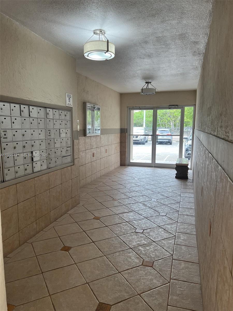 An indoor mailroom features tiled floors, wall-mounted mailboxes, and glass doors leading to a parking lot — 5501 NW 7th St # E219, Miami FL 33126, MIAMI, FL