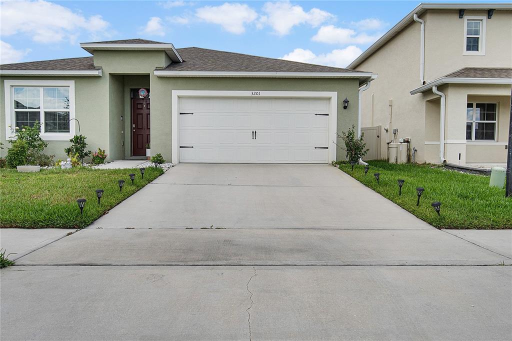 A single-story house with a green stucco exterior, a two-car garage, and a concrete driveway — 3201 EASTGROVE TERRACE, SANFORD, FL