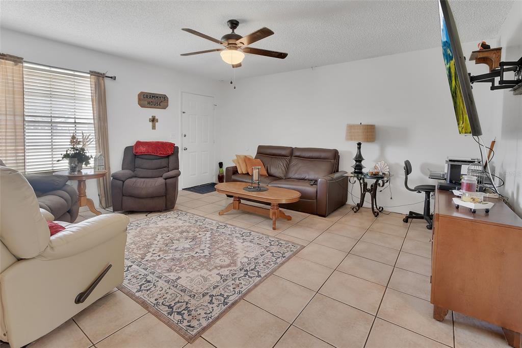 A living room features tile flooring, a ceiling fan, a brown sofa, and armchairs — 555 SANDY PINES DRIVE, ORANGE CITY, FL