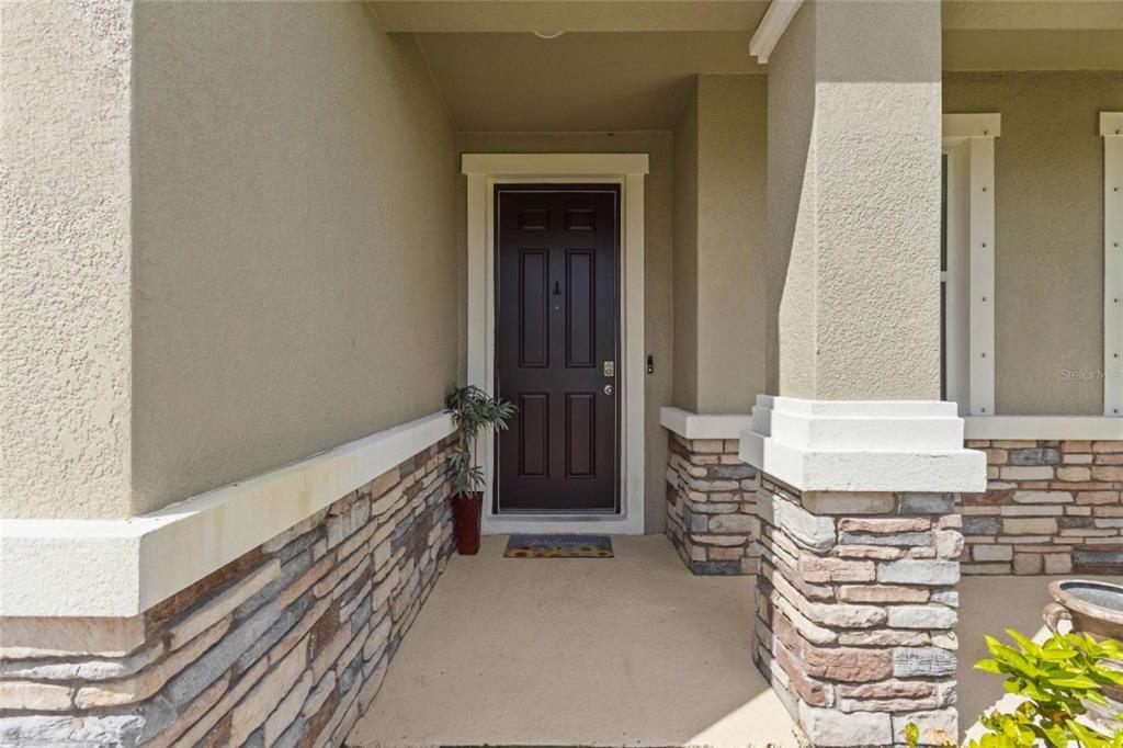 A covered front porch features a dark brown door, stone veneer siding, and a concrete floor — 3830 LIVELY CORAL PLACE, BRADENTON, FL