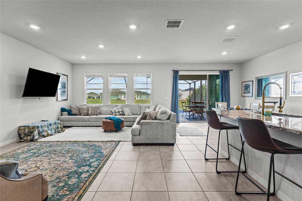 A spacious open-concept living room features a large sectional sofa, tile flooring, and a kitchen island — 3830 LIVELY CORAL PLACE, BRADENTON, FL