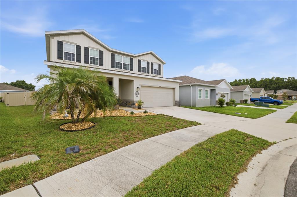 A two-story suburban house with a beige exterior, a two-car garage, and a palm tree — 10188 AGAVE COURT, LAND O LAKES, FL