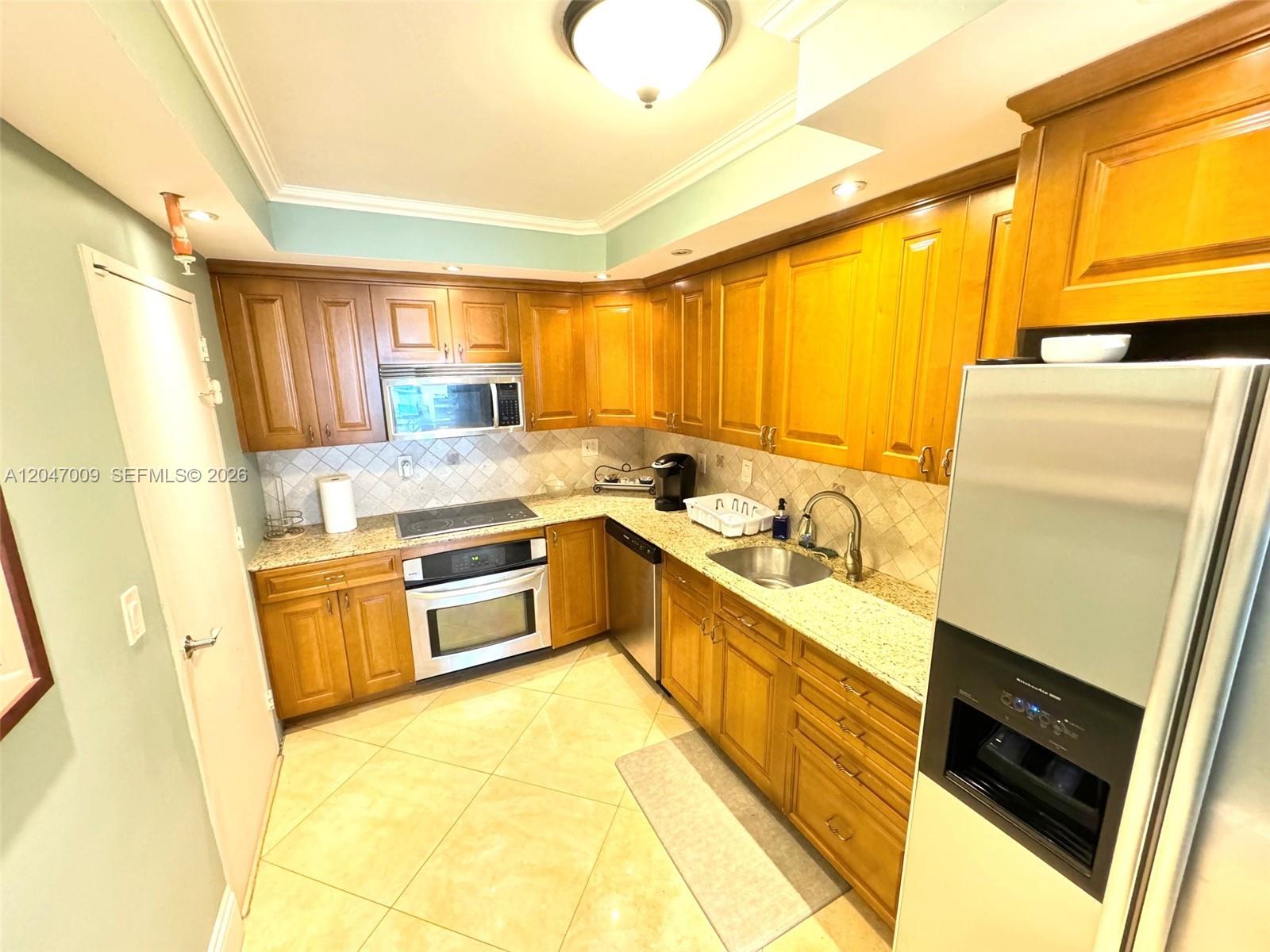 A kitchen features wood cabinets, granite countertops, stainless steel appliances, and light-colored tile flooring — 3901 S Ocean Dr # 7O, Hollywood FL 33019, HOLLYWOOD, FL
