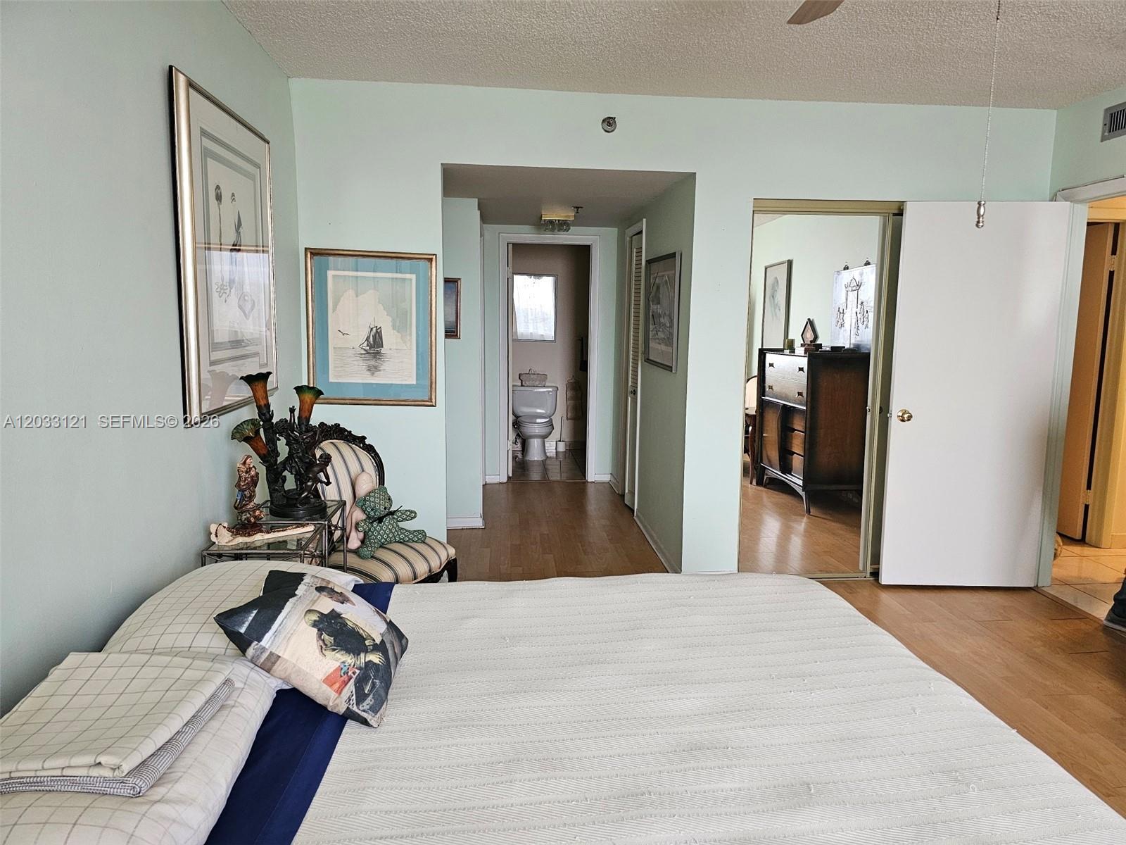 A bedroom features a bed, a small striped chair, and a doorway leading to a bathroom — 3850 Washington St # 1011, Hollywood FL 33021, HOLLYWOOD, FL