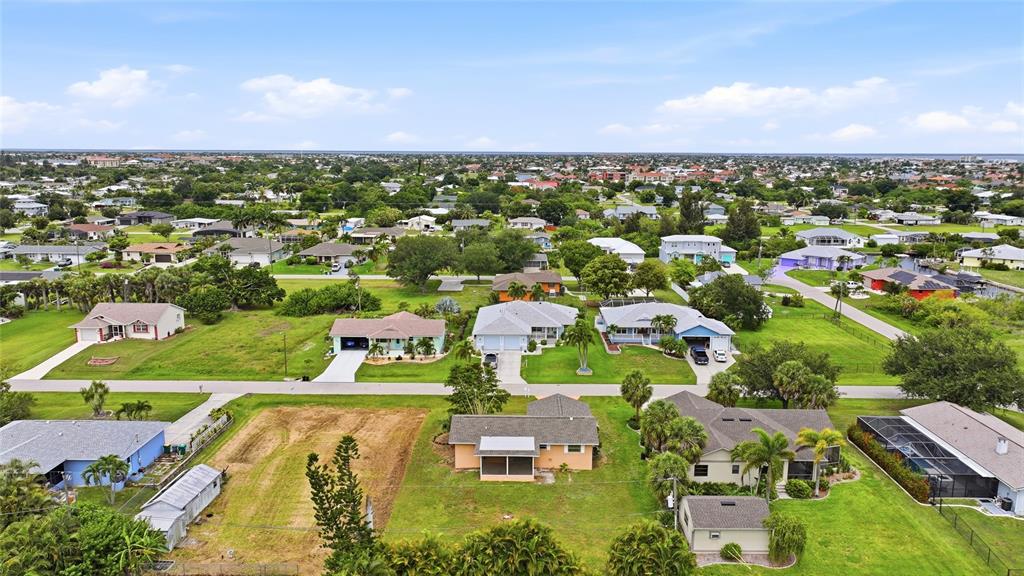 An aerial view shows a residential neighborhood with single-family homes, green lawns, and vacant lots — 2620 WISTERIA PLACE, PUNTA GORDA, FL