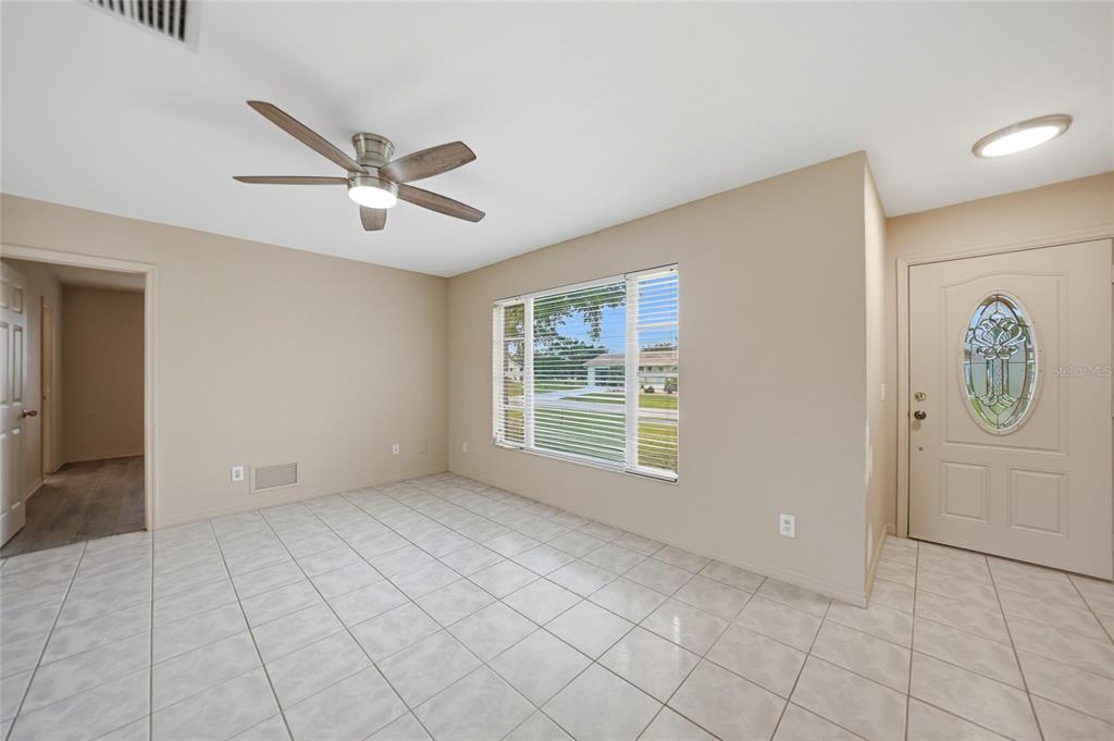 A room with beige walls, light tile flooring, a ceiling fan, and a front door — 2620 WISTERIA PLACE, PUNTA GORDA, FL
