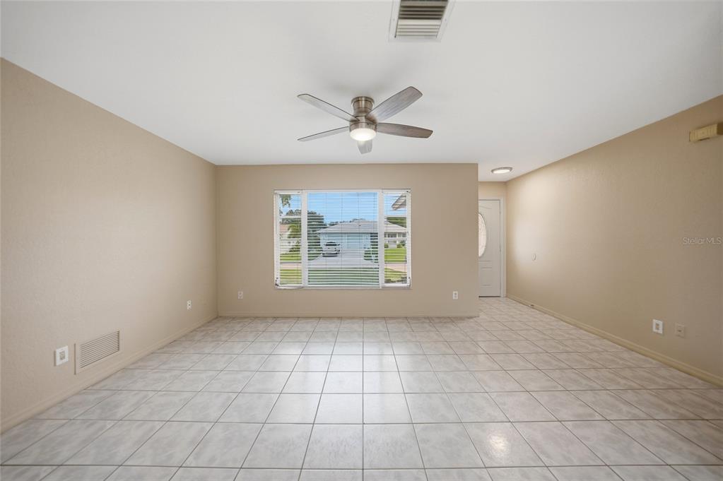 An empty room with beige walls, light-colored tile flooring, a ceiling fan, and a window — 2620 WISTERIA PLACE, PUNTA GORDA, FL