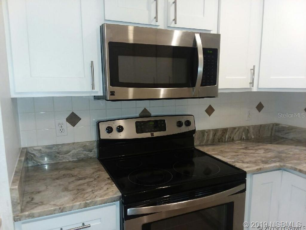 A kitchen features white cabinets, a stainless steel microwave, a black stove, and marble-patterned countertops — 572 PALM DRIVE, NEW SMYRNA BEACH, FL