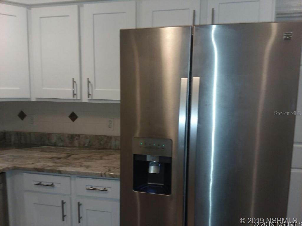 A stainless steel refrigerator stands next to white cabinets and a granite countertop — 572 PALM DRIVE, NEW SMYRNA BEACH, FL