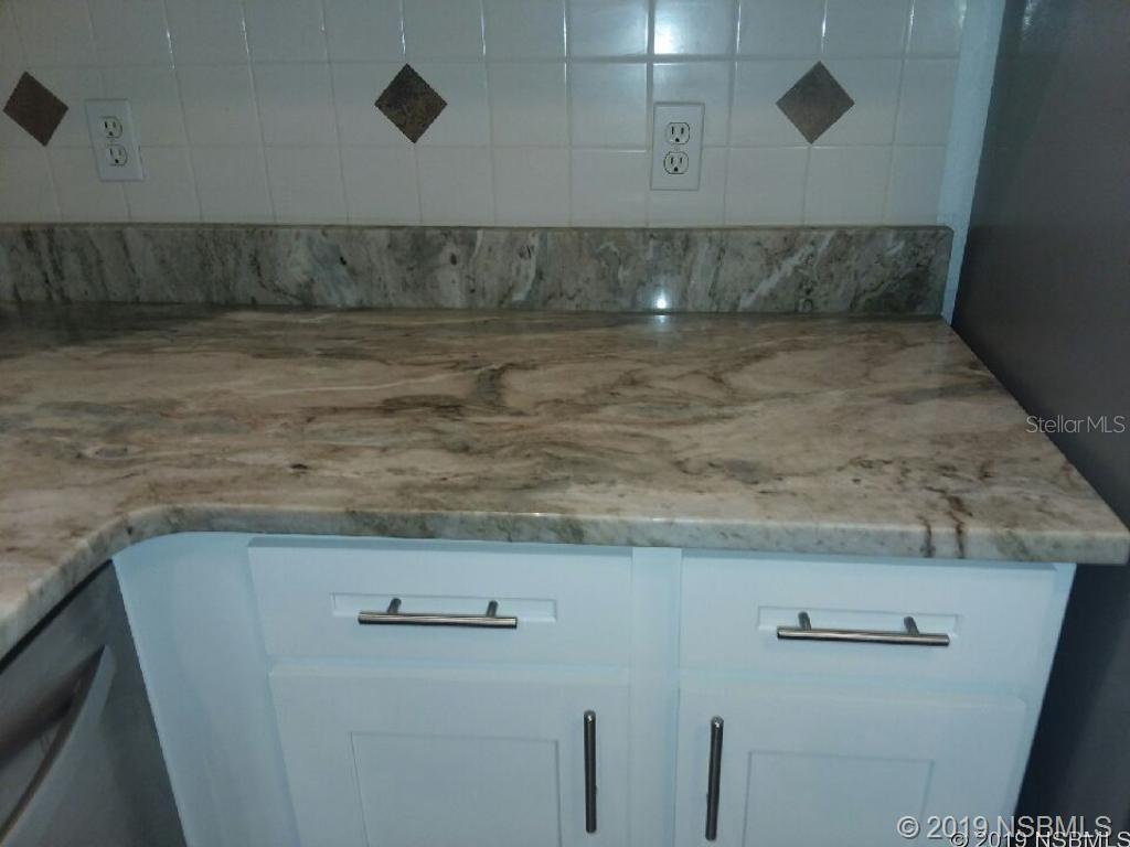 A kitchen counter features white cabinets, a stone countertop, and a tiled backsplash — 572 PALM DRIVE, NEW SMYRNA BEACH, FL