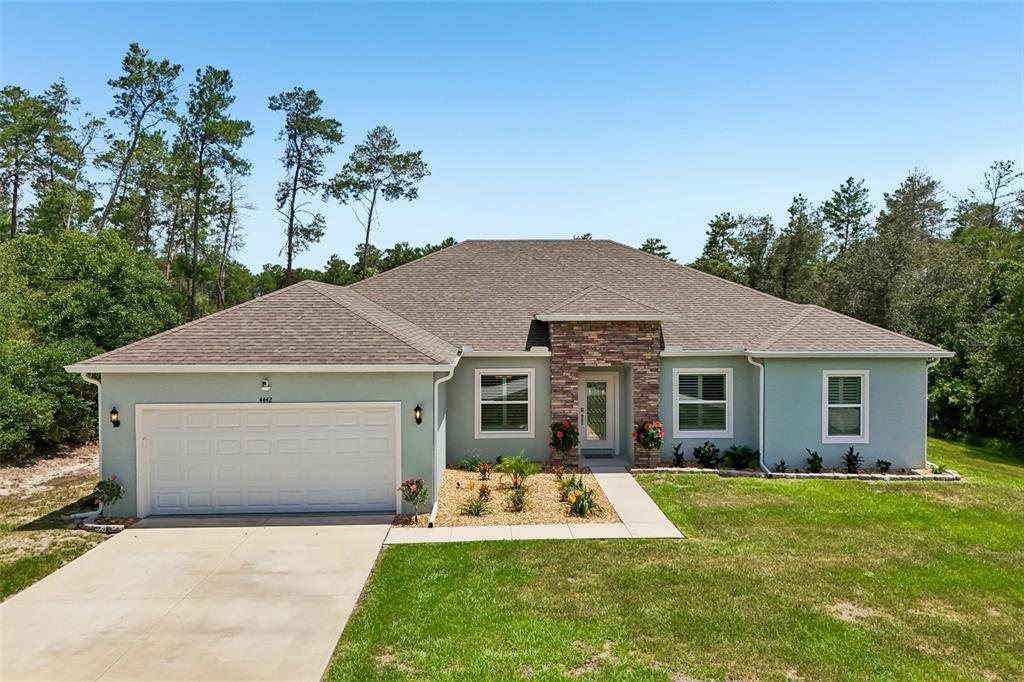 A single-story house with a light green stucco exterior, stone facade, and a two-car garage — 4442 SW 111TH PLACE, OCALA, FL
