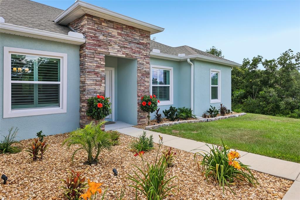 The exterior of a light blue house features a stone-accented entryway and landscaped garden beds — 4442 SW 111TH PLACE, OCALA, FL