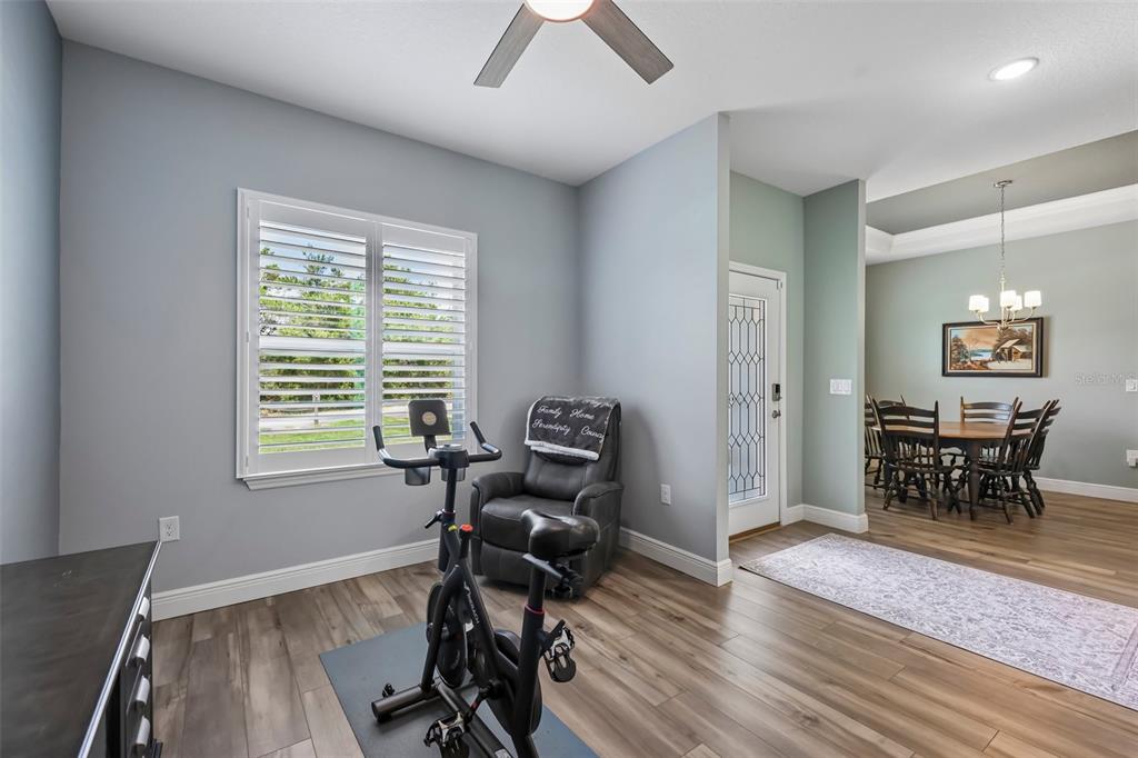 A room with light blue walls, wood-look flooring, a stationary bike, and an adjacent dining area — 4442 SW 111TH PLACE, OCALA, FL