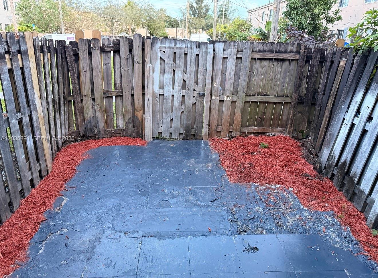 A small outdoor patio features dark painted tiles surrounded by red mulch and wooden fencing — 8447 NW 4th Ave # 8447, Miami FL 33150, MIAMI, FL