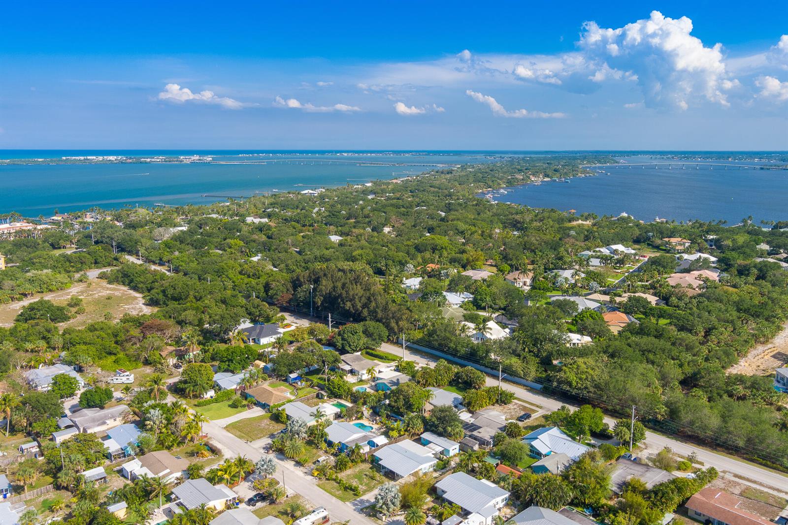 An aerial view shows a residential neighborhood surrounded by lush trees and nearby coastal waters — 2574 NE Roberta Street, Jensen Beach FL 34957, JENSEN BEACH, FL