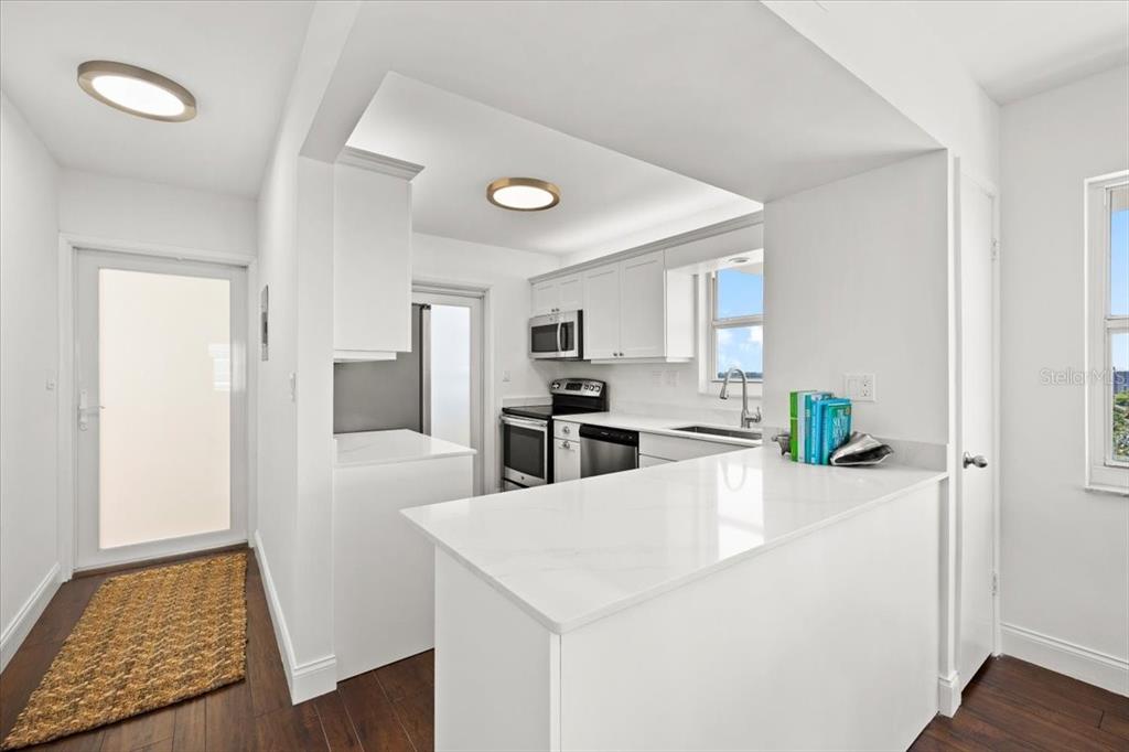 A bright kitchen features white cabinets, quartz countertops, and dark wood flooring — 1630 N OCEAN BLVD UNIT 1011, POMPANO BEACH, FL
