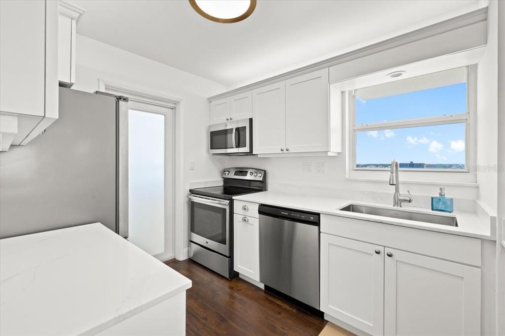 A kitchen features white cabinets, stainless steel appliances, a window, and dark wood flooring — 1630 N OCEAN BLVD UNIT 1011, POMPANO BEACH, FL