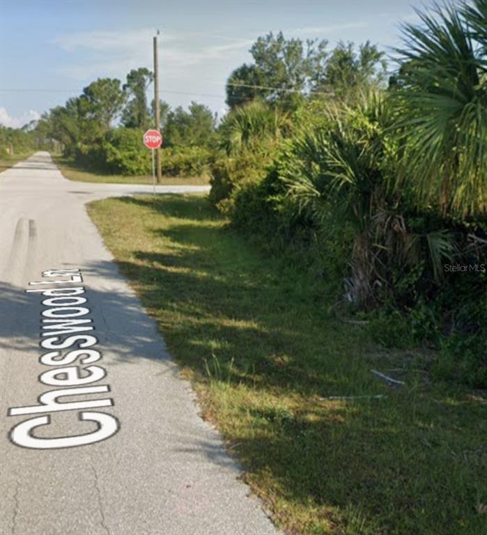 A paved road named Chesswood Lane leads to a stop sign near dense green vegetation — 14052 CHESSWOOD LANE, PORT CHARLOTTE, FL