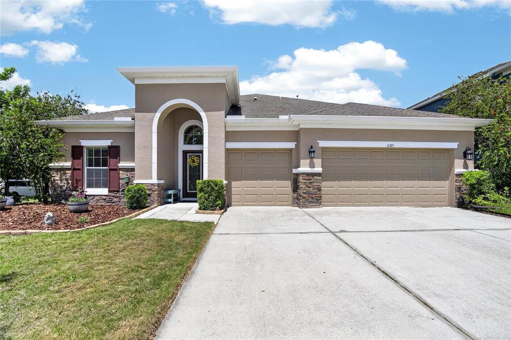 A single-story house features a tan stucco exterior, stone accents, and a three-car garage — 11321 SCRIBNER STATION LANE, LITHIA, FL
