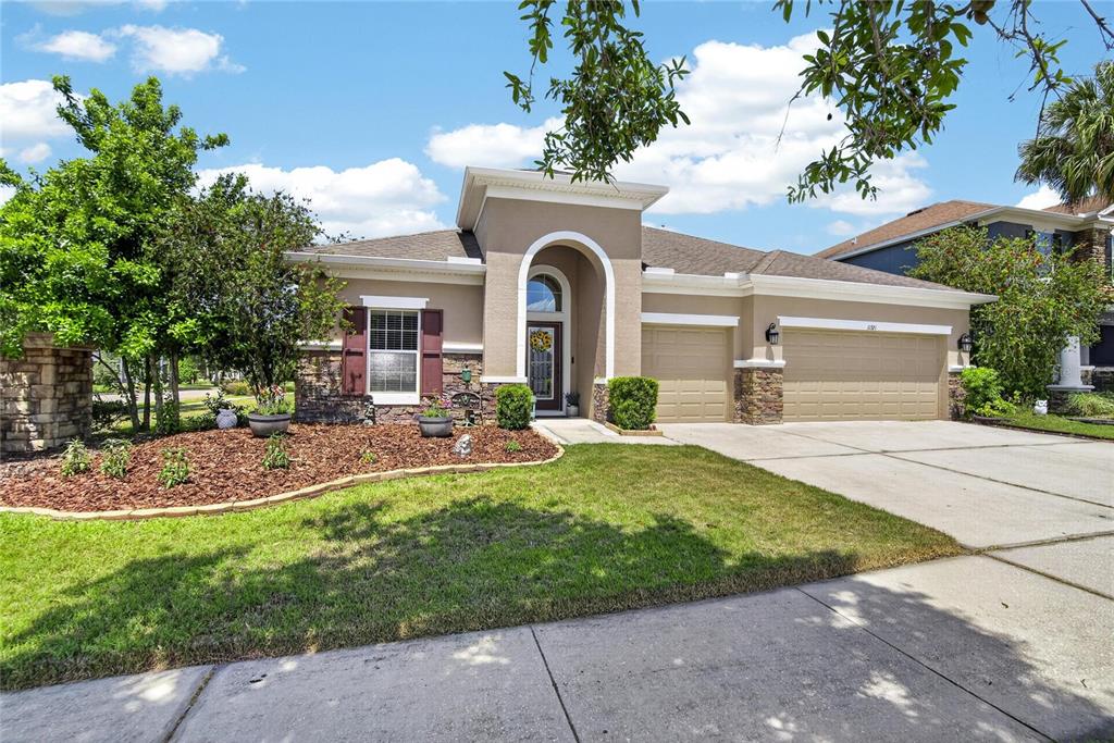 A single-story house features a tan stucco exterior, stone accents, and a three-car garage — 11321 SCRIBNER STATION LANE, LITHIA, FL