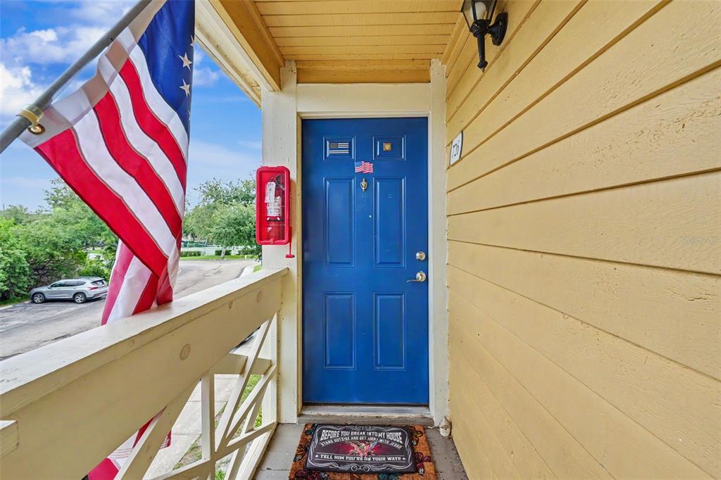 A blue front door with a fire extinguisher and an American flag on the porch — 115 112TH AVENUE NE UNIT 726, ST PETERSBURG, FL