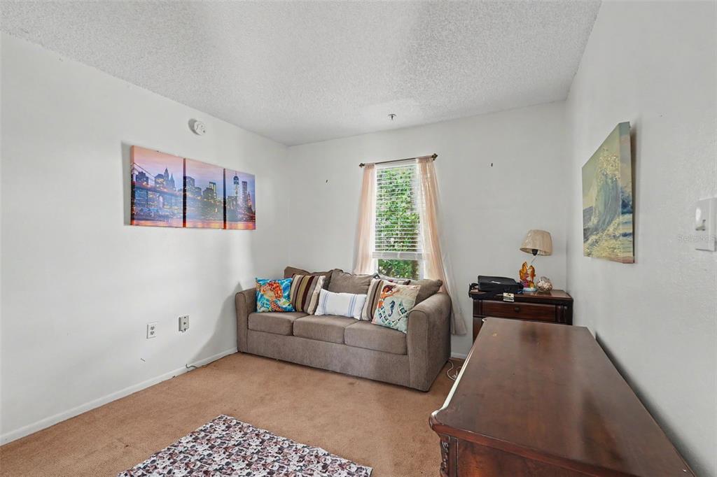 A living room features a brown sofa, a window with curtains, and a wooden dresser — 115 112TH AVENUE NE UNIT 726, ST PETERSBURG, FL