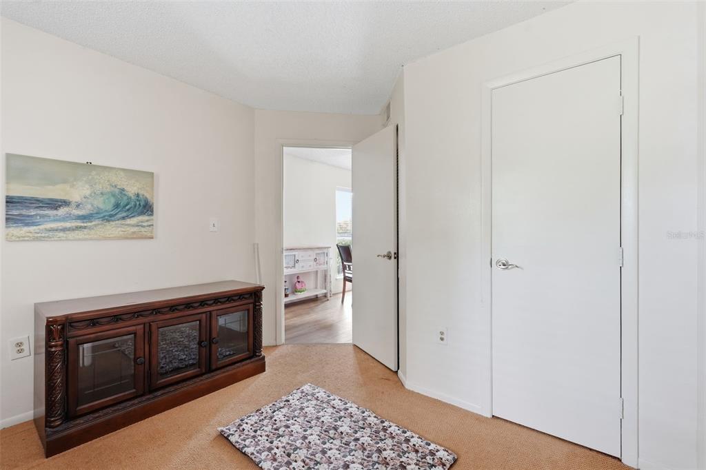 A room with tan carpet, a dark wood cabinet, a wall painting, and an open doorway — 115 112TH AVENUE NE UNIT 726, ST PETERSBURG, FL