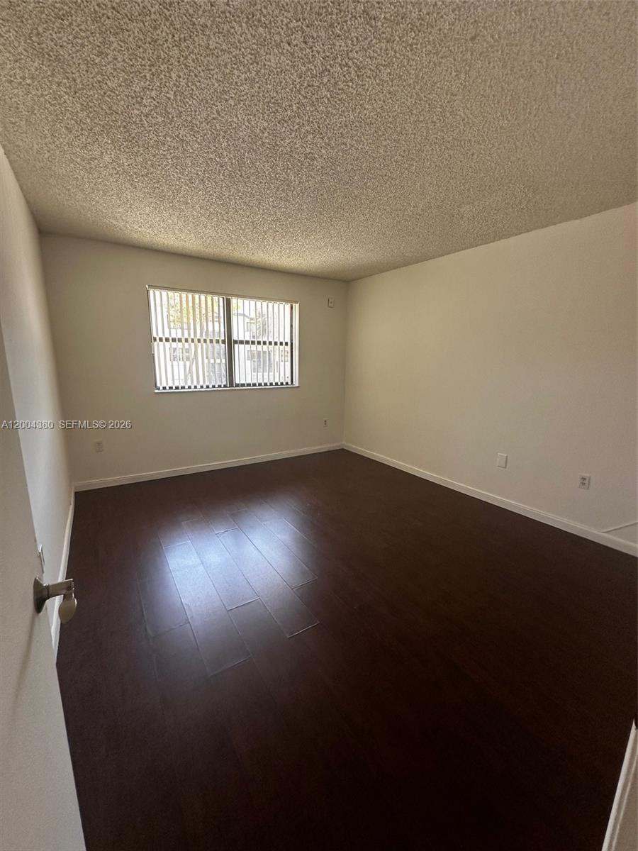 An empty room features dark wood-look flooring, white walls, and a window with blinds — 7220 NW 179th St # 201, Hialeah FL 33015, HIALEAH, FL