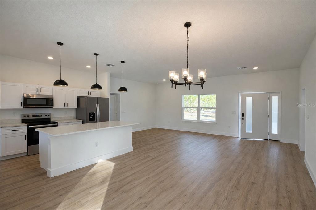 An open-concept kitchen and living area featuring white cabinets, stainless appliances, and wood-look flooring — 3566 W HAYWARD LANE, CITRUS SPRINGS, FL