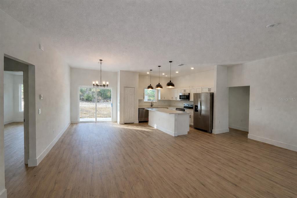 An open-concept kitchen and dining area features light wood flooring, white cabinetry, and stainless appliances — 3566 W HAYWARD LANE, CITRUS SPRINGS, FL