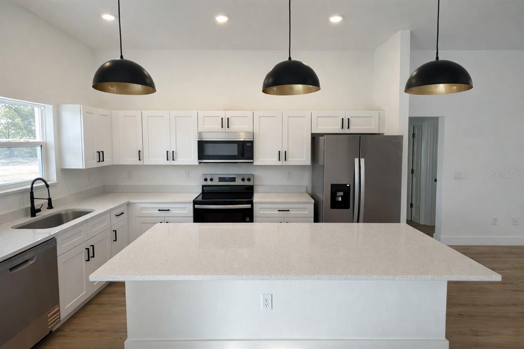 A modern kitchen features white cabinets, stainless steel appliances, a quartz island, and pendant lighting — 3566 W HAYWARD LANE, CITRUS SPRINGS, FL