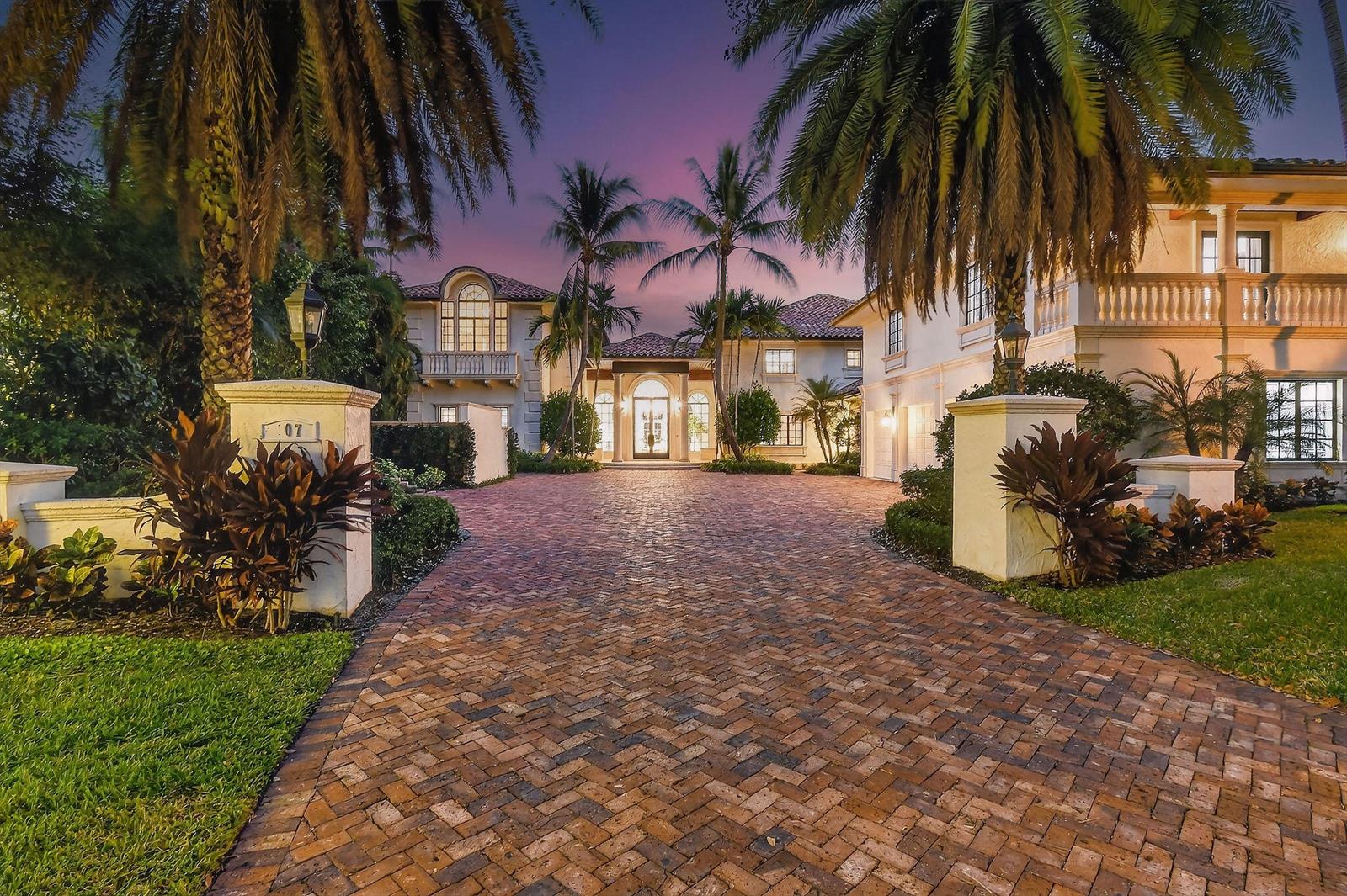 A large, two-story Mediterranean-style house with a brick driveway and palm trees at dusk — 107 Schooner Lane, Jupiter FL 33477, JUPITER, FL