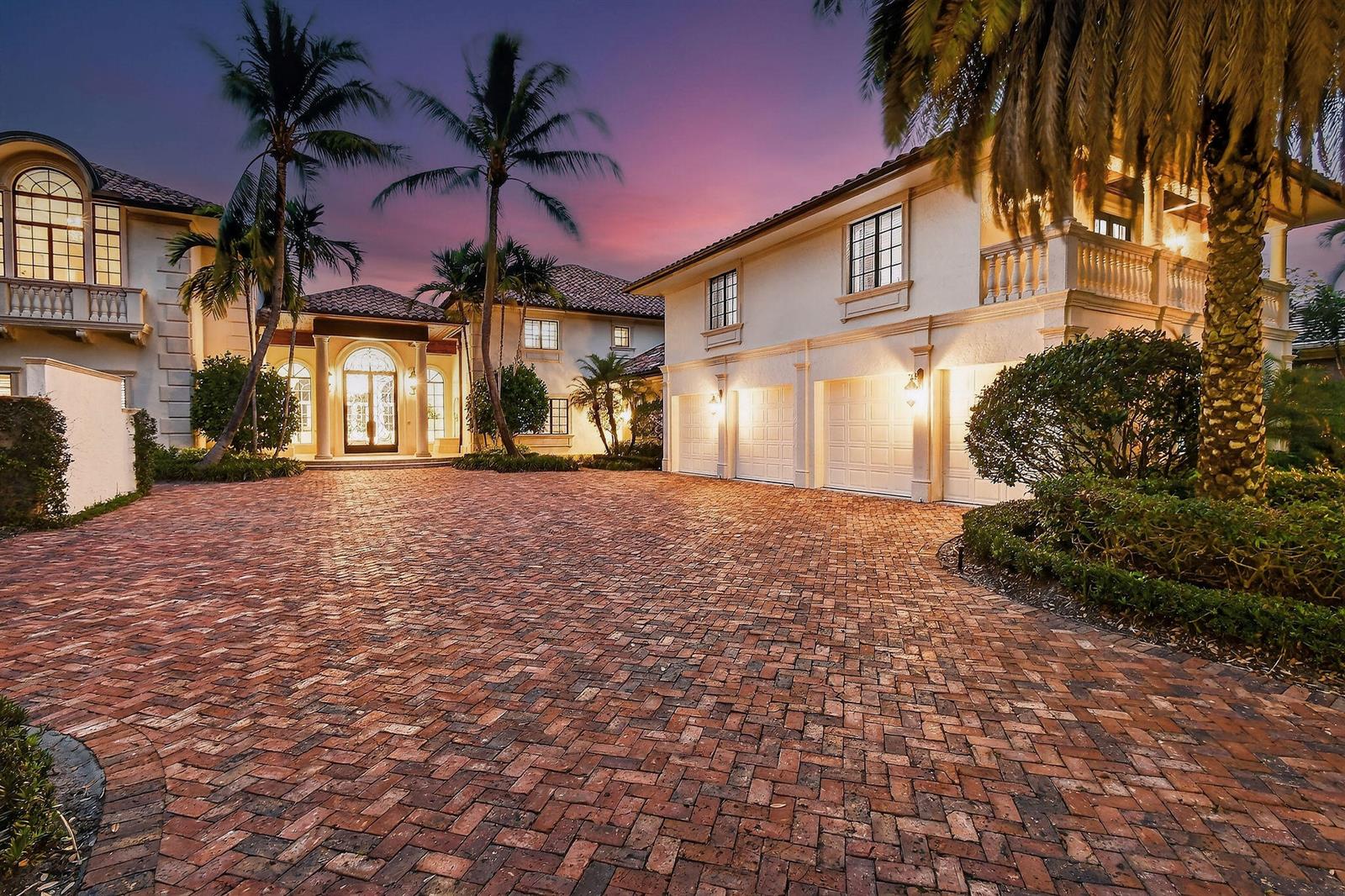 A large two-story house with a brick driveway, three-car garage, and palm trees at dusk — 107 Schooner Lane, Jupiter FL 33477, JUPITER, FL