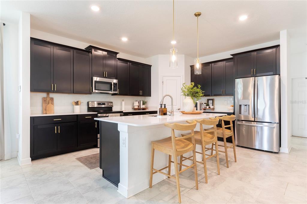 A modern kitchen features black cabinets, white countertops, a central island, and stainless steel appliances — 2380 VOLUNTEER AVENUE, KISSIMMEE, FL