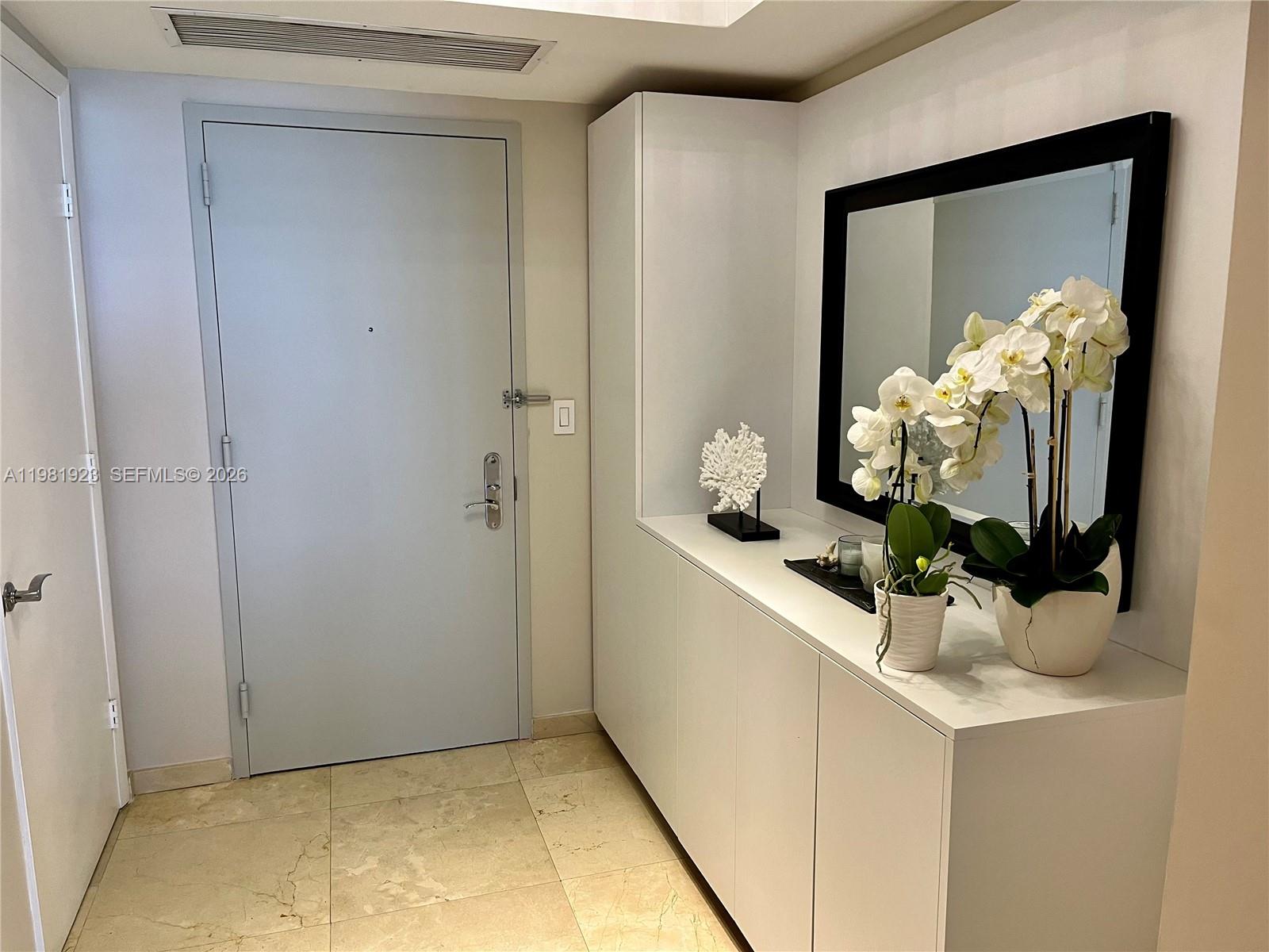 An entryway features a light gray door, white cabinetry, a mirror, and potted orchids — 1830 S Ocean Dr # 4004, Hallandale Beach FL 33009, HALLANDALE BEACH, FL