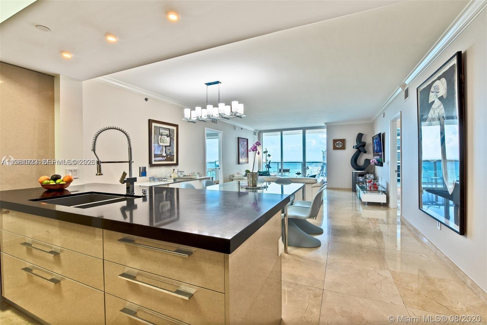 A modern kitchen with dark countertops overlooks a dining area and a bright living space — 1830 S Ocean Dr # 4004, Hallandale Beach FL 33009, HALLANDALE BEACH, FL