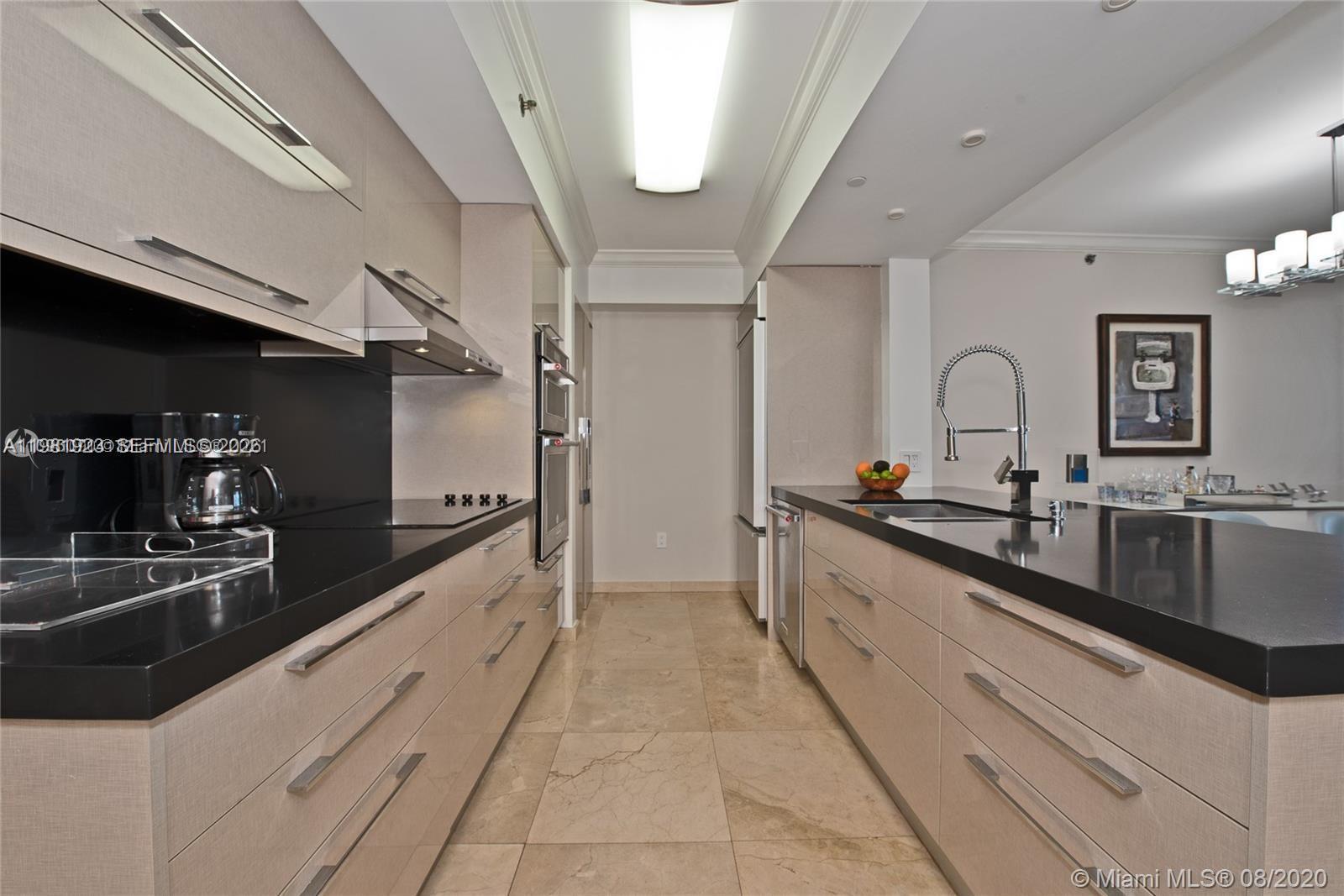 A modern galley kitchen features light wood cabinetry, black countertops, and beige tile flooring — 1830 S Ocean Dr # 4004, Hallandale Beach FL 33009, HALLANDALE BEACH, FL