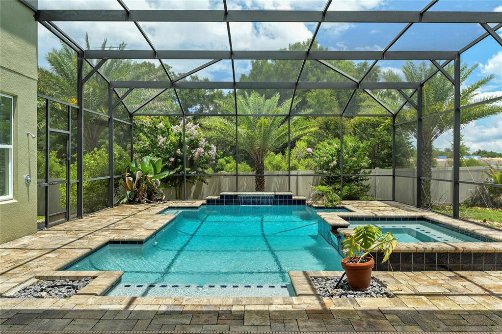 A screened-in swimming pool and hot tub with stone pavers and lush tropical landscaping — 4473 BERRY OAK DRIVE, APOPKA, FL