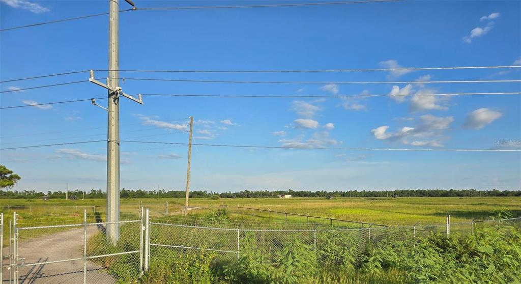 A fenced, grassy lot features utility poles and power lines under a blue sky — INTERNATIONAL DRIVE, ORLANDO, FL