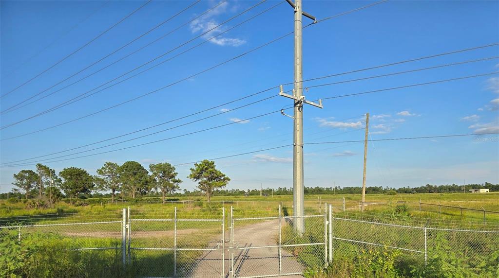 A chain-link gate opens to a gravel path leading into a grassy, open field — INTERNATIONAL DRIVE, ORLANDO, FL