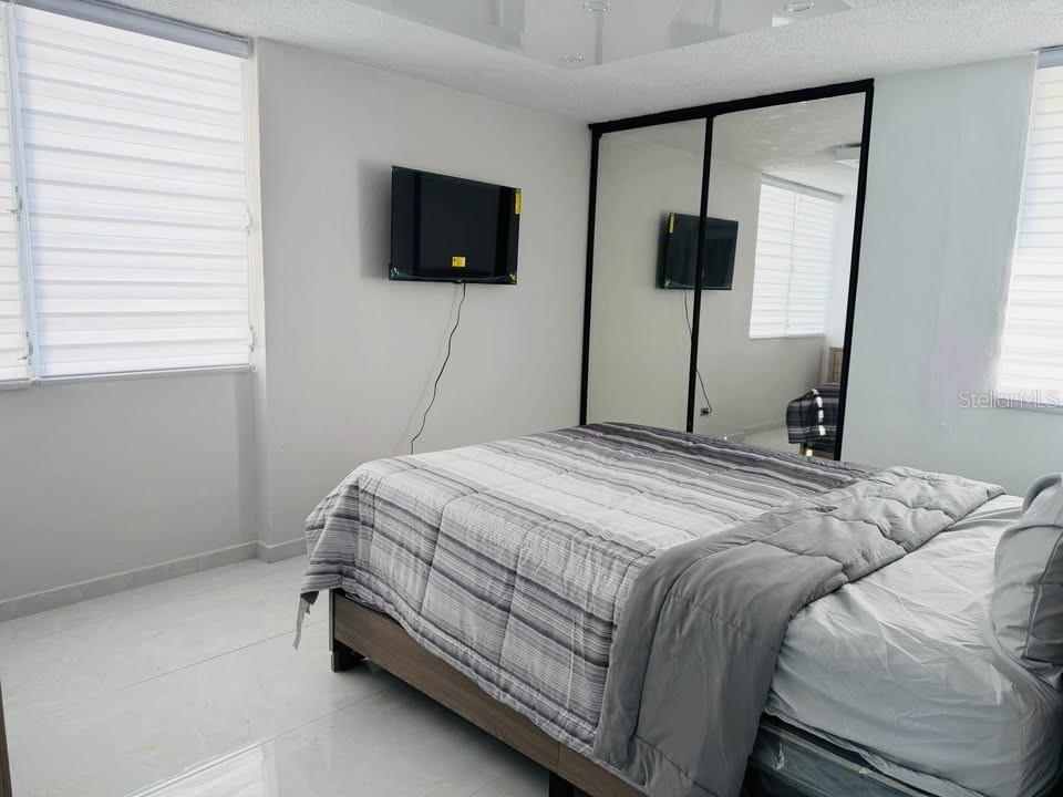 A bedroom features a bed, a wall-mounted television, and mirrored closet doors — Dos Marinas II DOS MARINAS II, NO. 110, FAJARDO, PR
