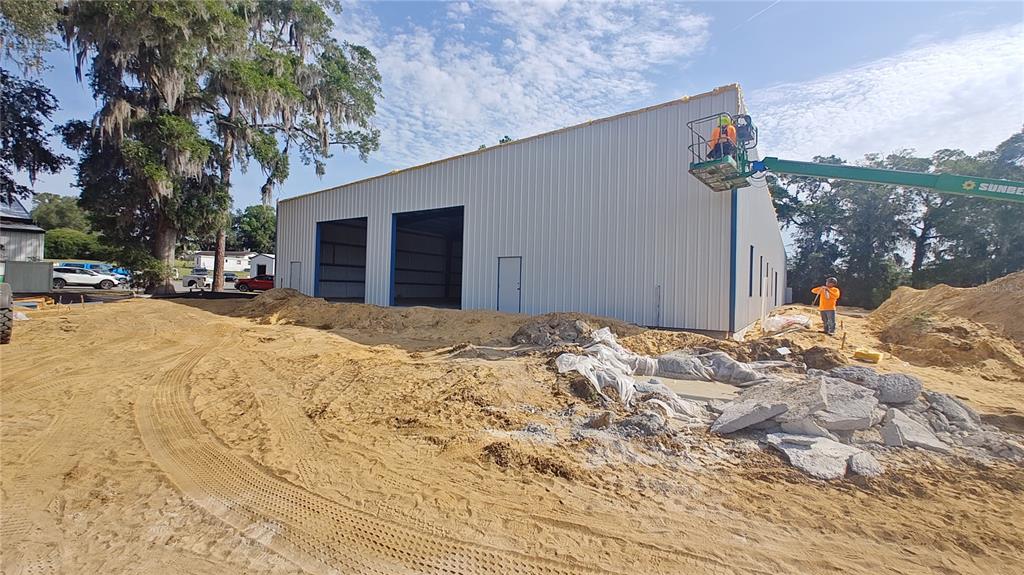 A metal warehouse building under construction stands on a sandy lot with workers present — 12142 SE COUNTY 484 HIGHWAY, BELLEVIEW, FL