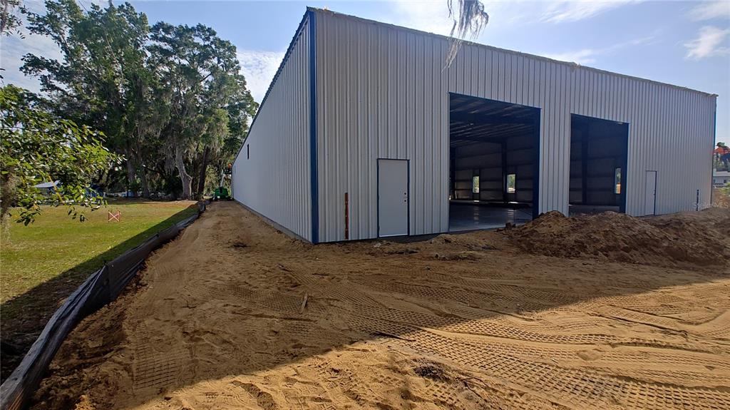 A large, unfinished metal warehouse building sits on a sandy lot with construction debris — 12142 SE COUNTY 484 HIGHWAY, BELLEVIEW, FL