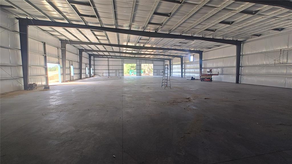 An expansive, empty warehouse interior features a concrete floor, metal walls, and exposed steel beams — 12142 SE COUNTY 484 HIGHWAY, BELLEVIEW, FL