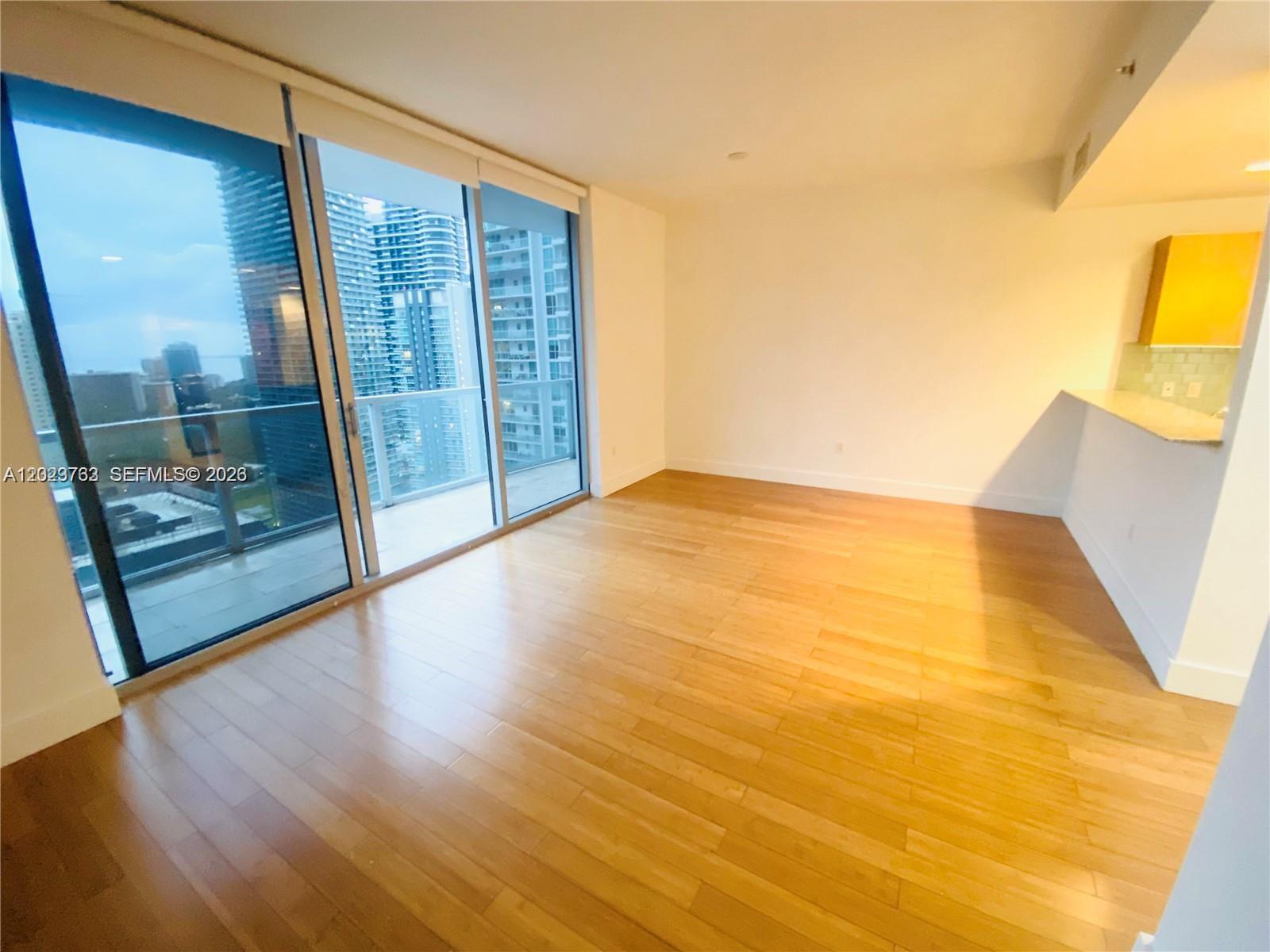An empty room features light wood flooring, floor-to-ceiling windows, and an adjacent kitchen area — 1060 Brickell Ave # 3109, Miami FL 33131, MIAMI, FL