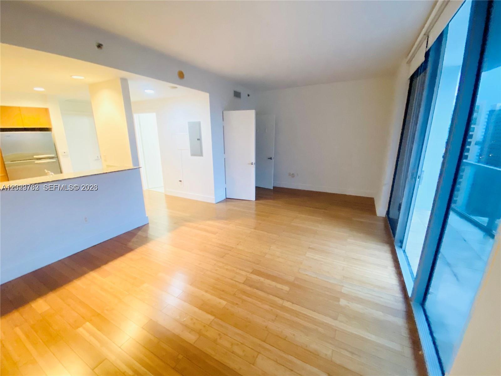 An unfurnished living area features light wood flooring, white walls, and a sliding glass door — 1060 Brickell Ave # 3109, Miami FL 33131, MIAMI, FL