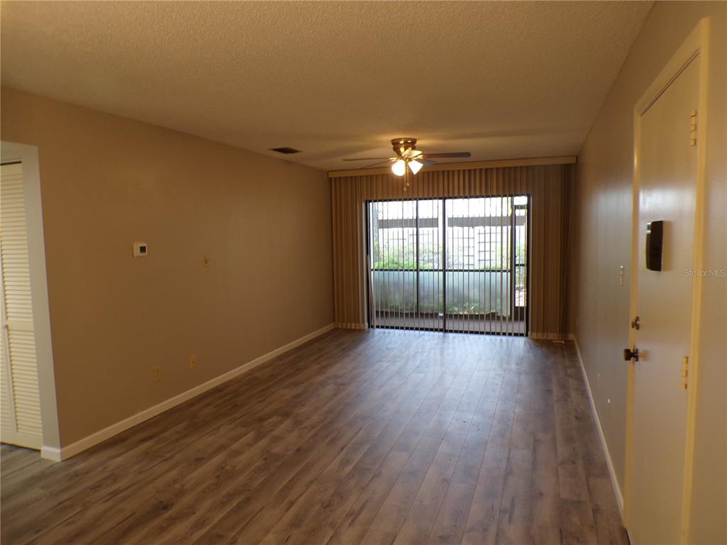 An empty living room features wood-look flooring, a ceiling fan, and sliding glass patio doors — 622 BIRD BAY DRIVE S UNIT 103, VENICE, FL