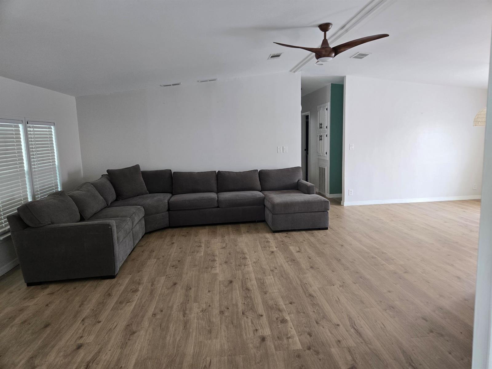 A living room features a large gray sectional sofa, light wood flooring, and a ceiling fan — 1699 SW 35th Circle, Okeechobee FL 34974, OKEECHOBEE, FL