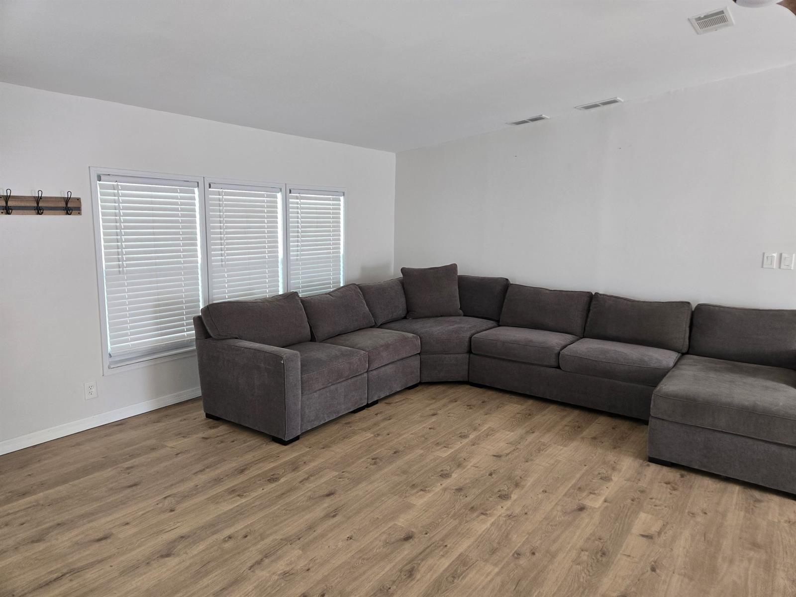 A living room features light wood-look flooring, white walls, and a large grey sectional sofa — 1699 SW 35th Circle, Okeechobee FL 34974, OKEECHOBEE, FL