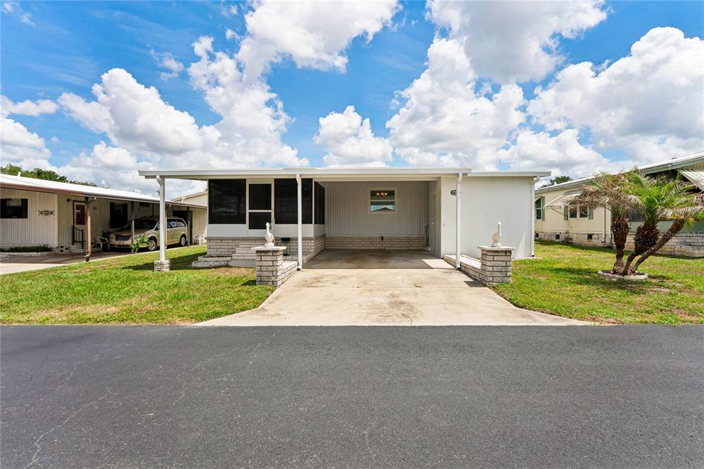 A single-story manufactured home with a carport, screened-in porch, and brick-accented pillars — 37537 PINATA AVENUE, ZEPHYRHILLS, FL